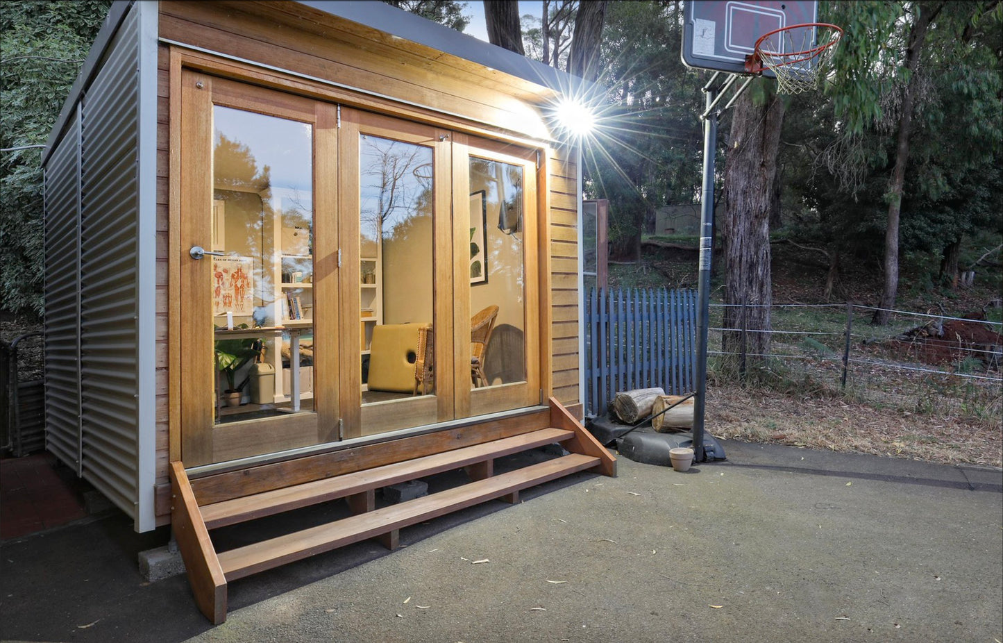 Hideaway garden studio with cedar cladding and bifold timber doors, installed beside a backyard basketball court — perfect for a home office or creative space.