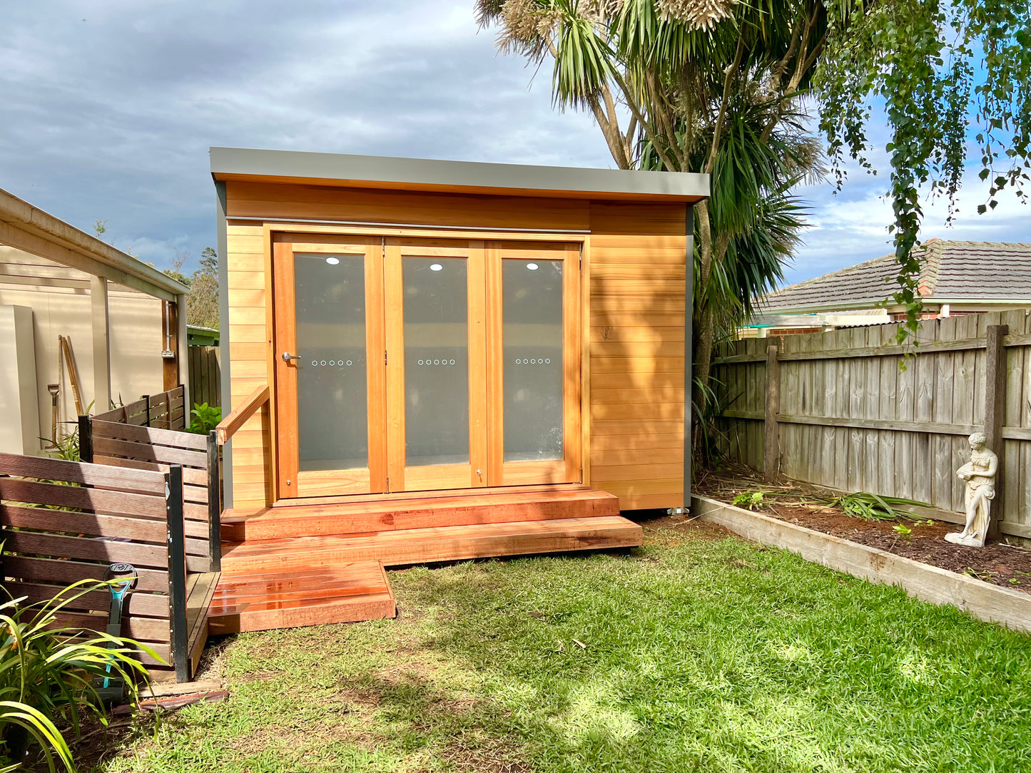 Designer Hideaways Hideout garden studio with cedar cladding and bifold doors, elevated on timber steps in a landscaped backyard.