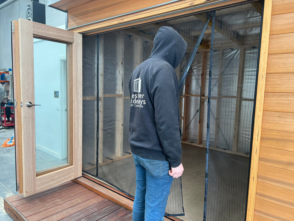 Retractable bug mesh screen being demonstrated on a timber garden studio door — ideal for keeping insects out while allowing airflow in backyard office pods and creative spaces.