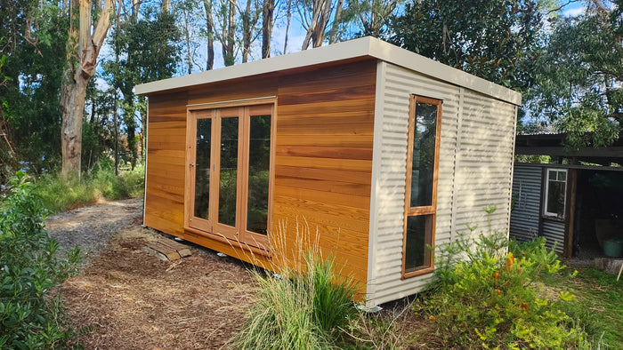 The Haven prefab garden studio with timber cladding and Colorbond steel siding, set in a native Australian garden — modern outdoor workspace or creative studio.