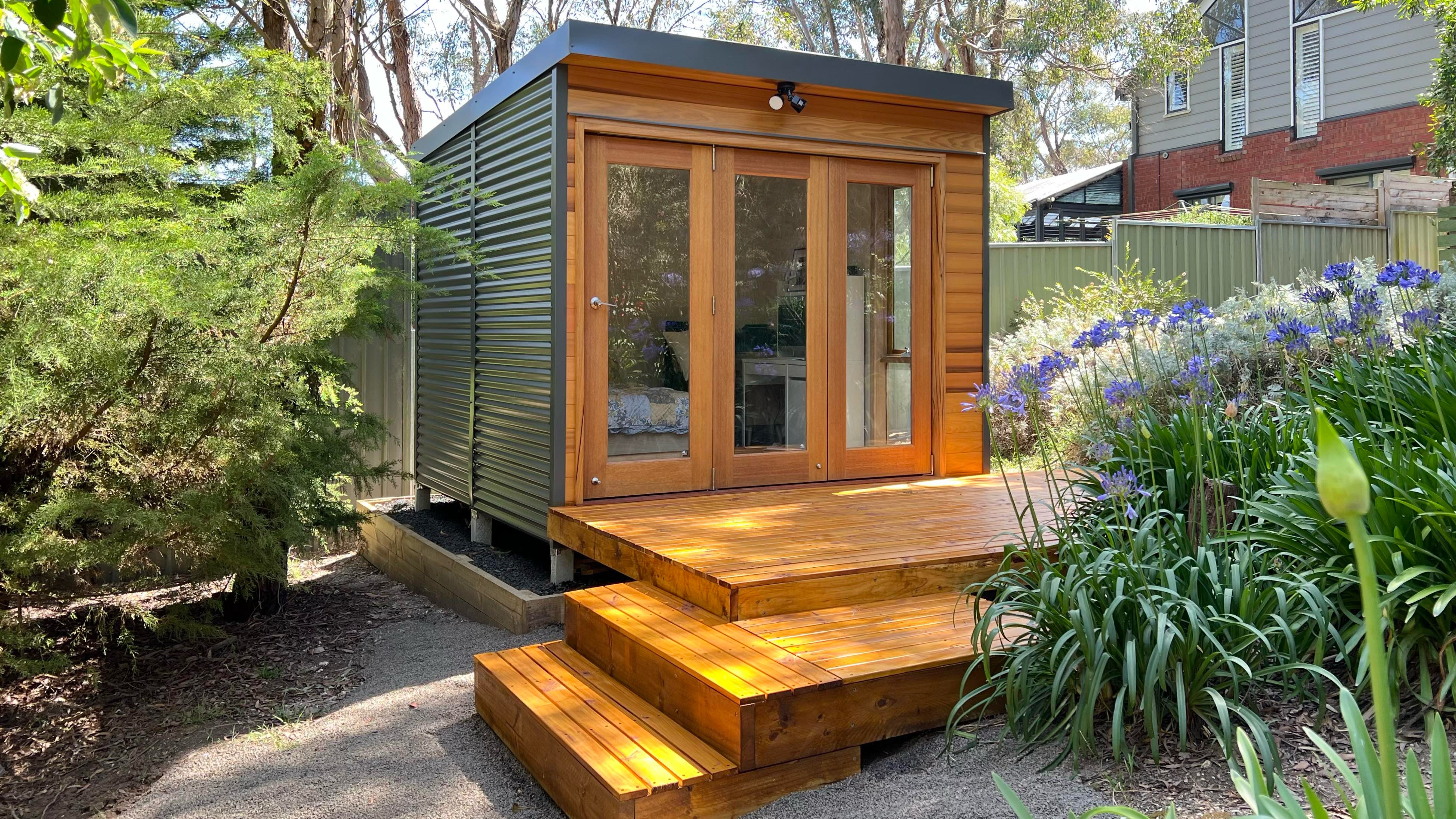 The Hideaway garden studio with timber steps and Colorbond cladding, set in a landscaped backyard. Ideal for a backyard office, artist’s retreat, or compact DIY studio pod.