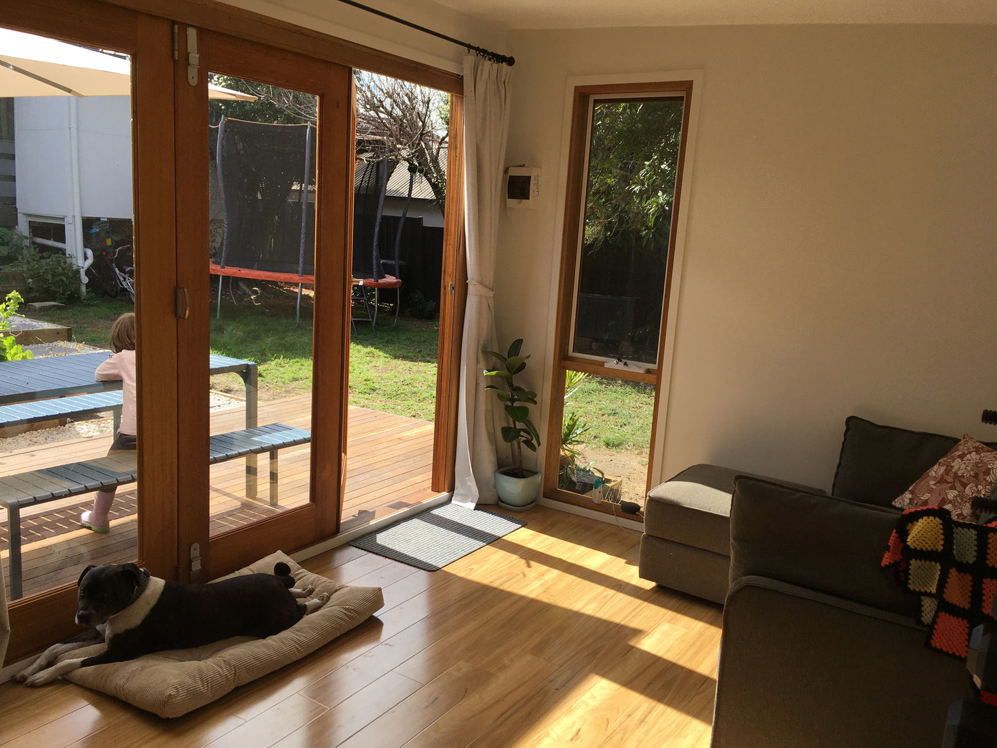 Interior of a garden studio with timber bifold doors and a timber awning window opening to a backyard deck, showing natural light, wooden flooring, and a relaxed living space.
